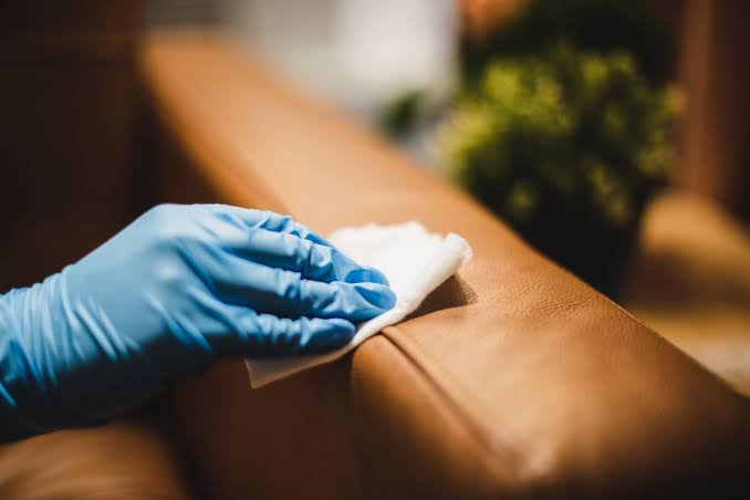 Gloved hand cleaning a leather sofa arm